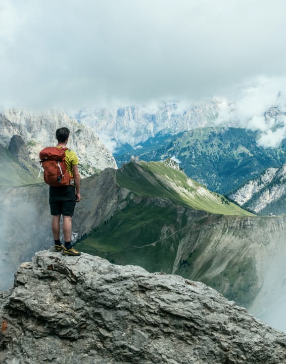 Hiker with a backpack stands on top of a mountain and looks at a panoramic view of the mountains.